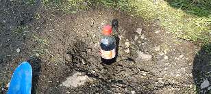 A small bottle of coke sitting in a pothole