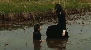 Screen capture from Fatal Frame showing the pond-walking girl kneeling down to another girl who is in the water up to her chest.